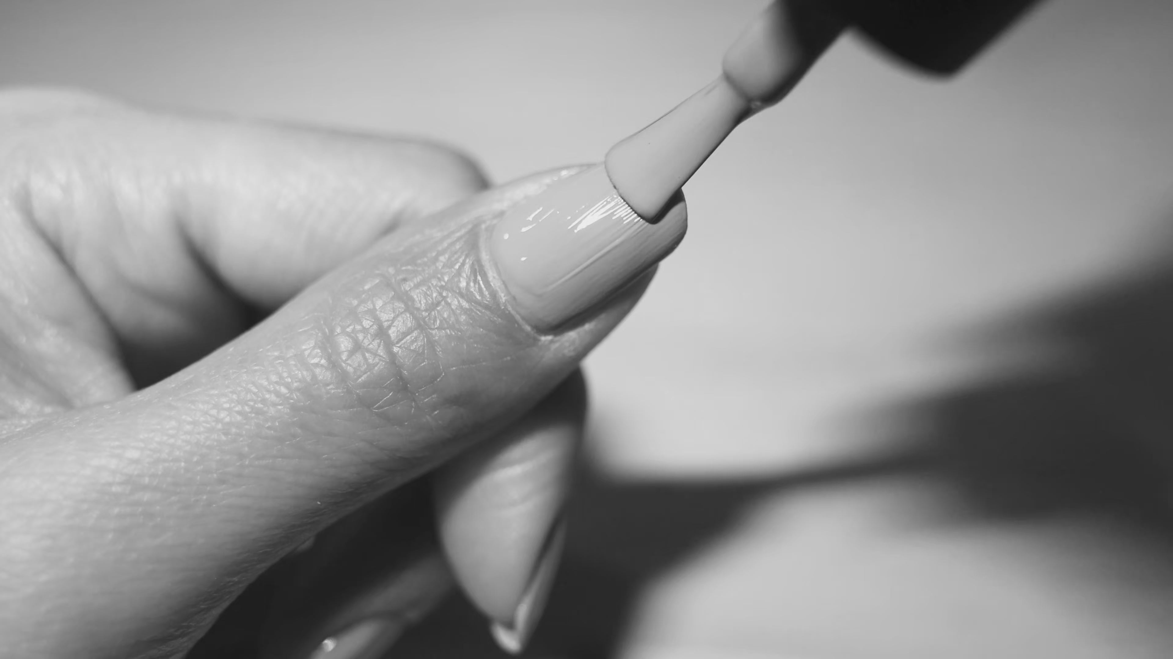 Close up black and white video of thumb nail being painted with nail polish brush